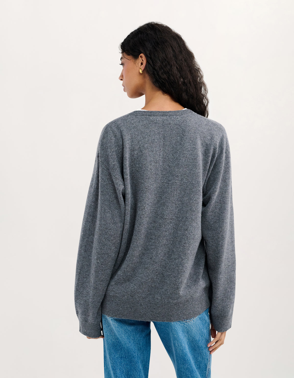 A woman shown from the back wearing a heather gray knit sweater and blue jeans against a plain light background.