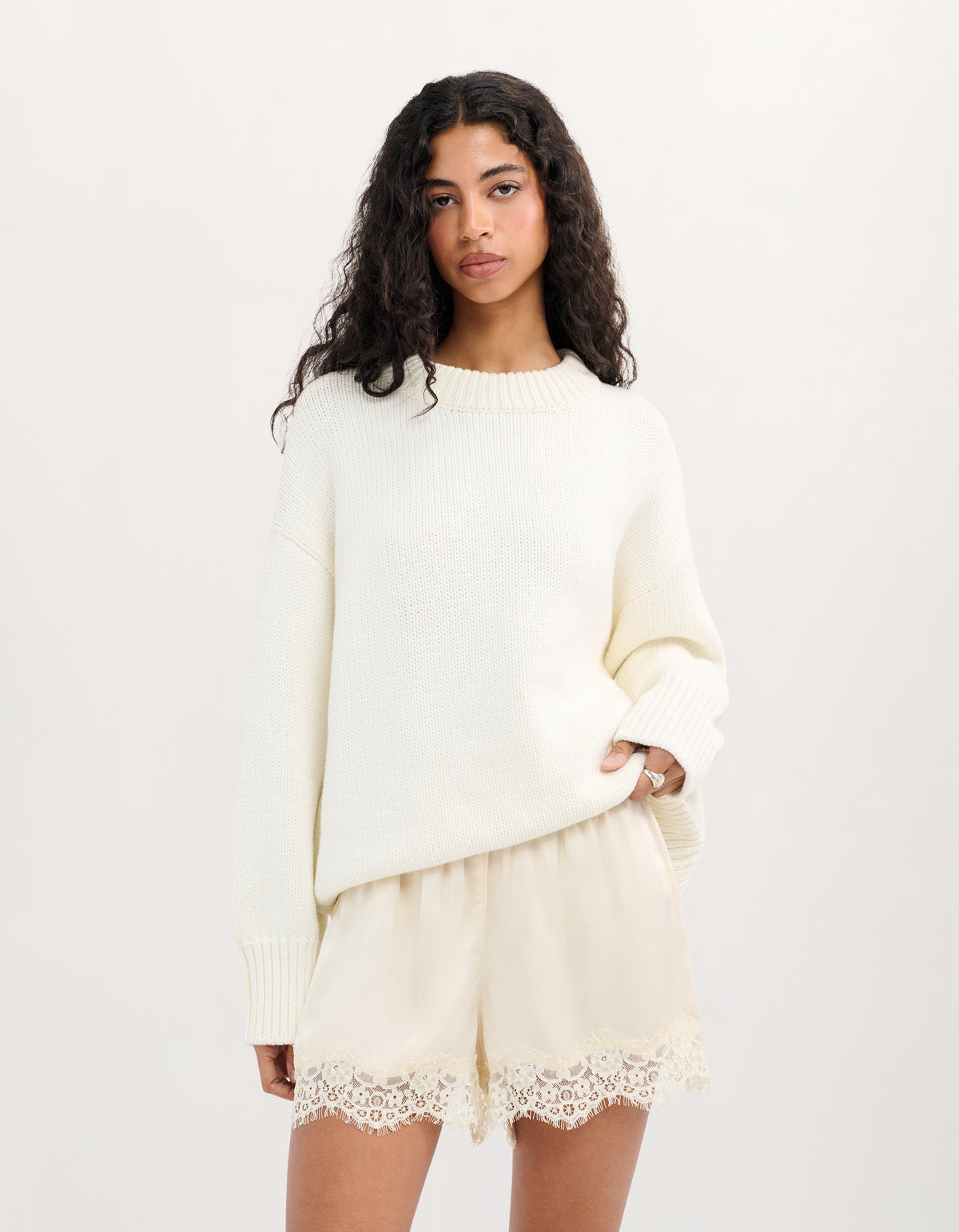 A woman modeling a cream-colored knit sweater and matching shorts with lace trim, photographed against a plain light background.