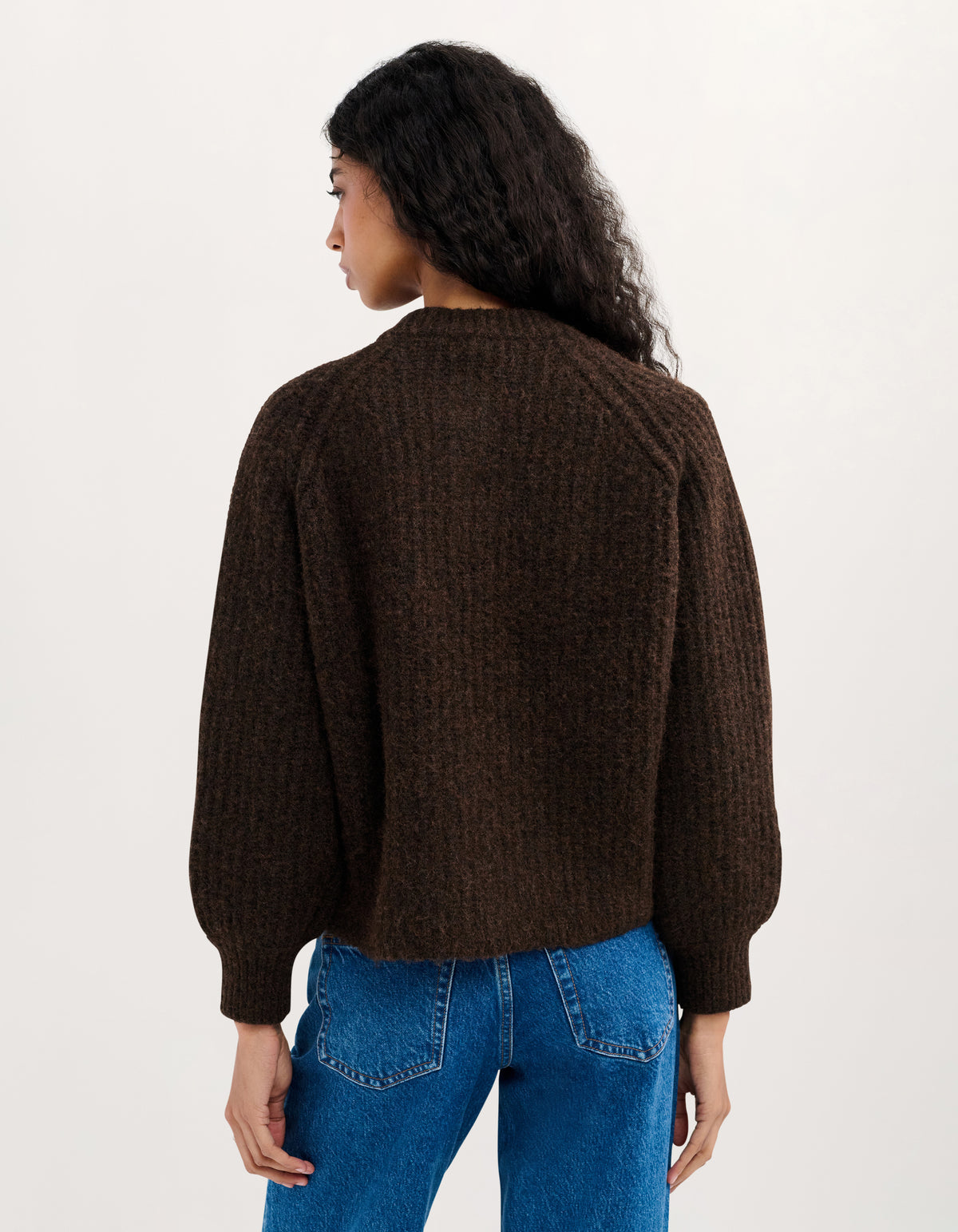 A woman shown from the back wearing a dark brown textured knit sweater and blue jeans against a plain light background.