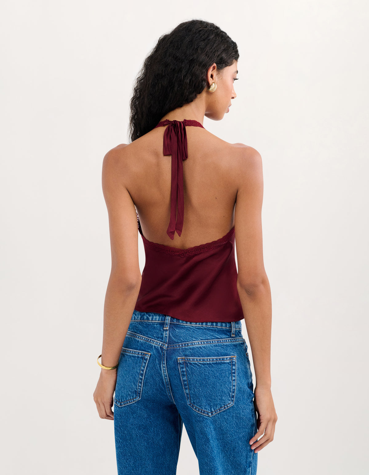 A woman shown from the back wearing a burgundy halter top with a tie-back detail and blue jeans, photographed against a plain light background.