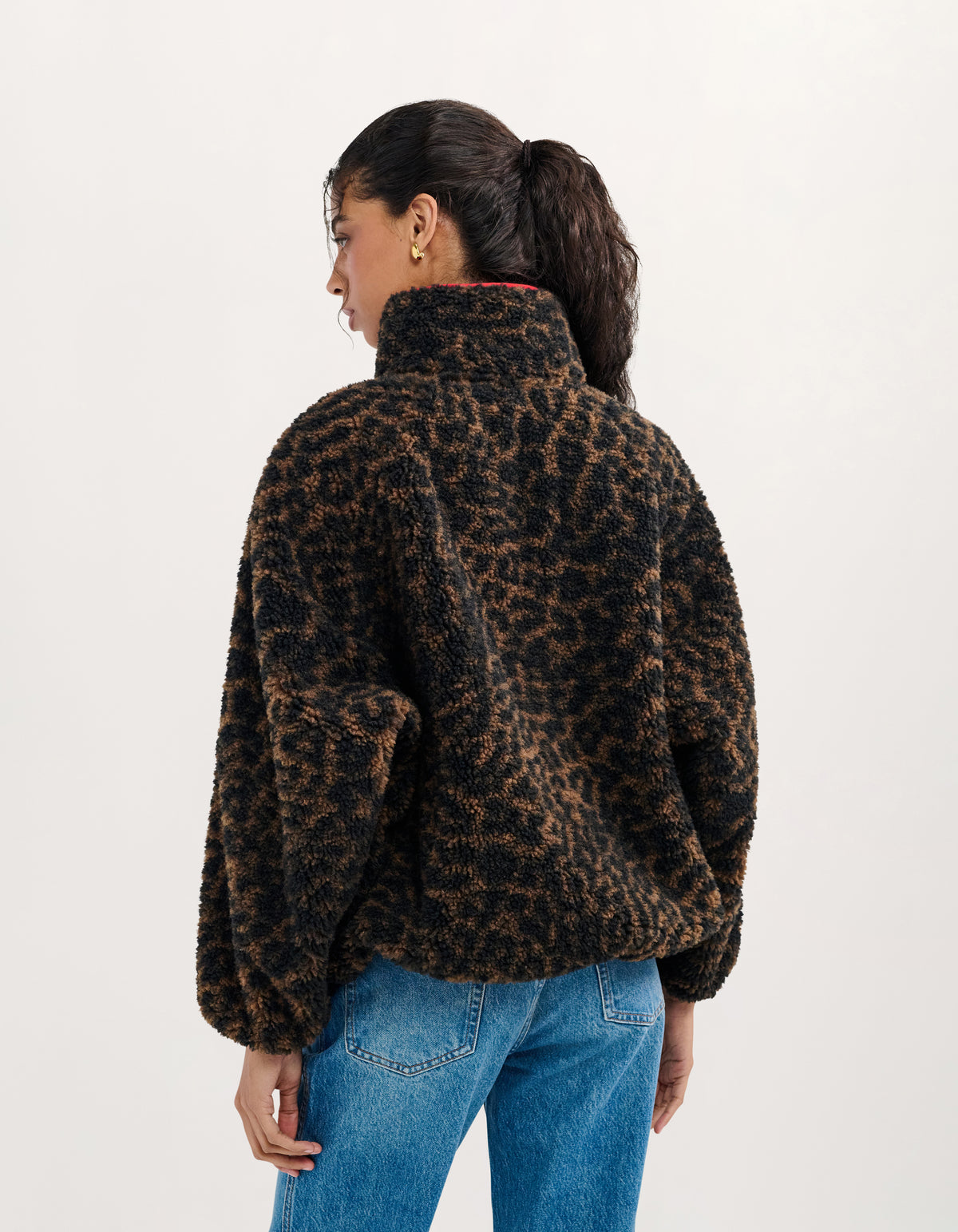 A woman shown from the back wearing a brown and black leopard-print fuzzy fleece jacket with blue jeans, photographed against a plain light background.